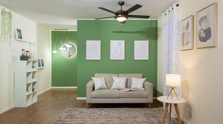 sala de estar con sofá crema frente a pared verde con cuadros blantos y ventilador de techo